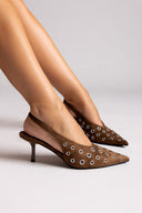 Brown high-heeled shoes with decorative studs worn by a person on a light background