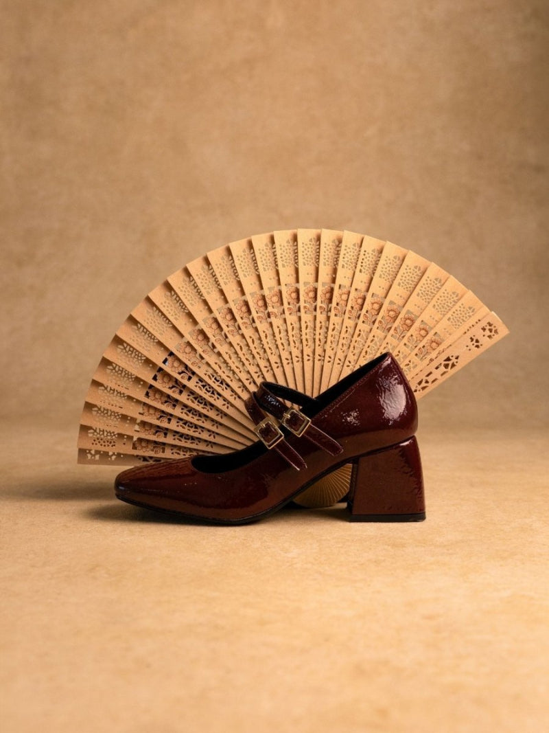 Brown shoe with a buckle next to a beige fan on a beige background
