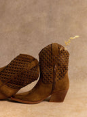 Pair of brown suede cowboy boots with woven detailing on a beige background